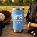 Blue tumbler with 'Baseball Mom Kevin #15' text on a wooden surface with baseball equipment.