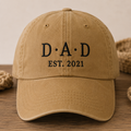 Brown cap with 'DAD EST. 2021' text on a wooden surface