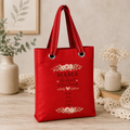 Red tote bag with floral design and text "MAMA The Heart of Our Family" and kids names on a wooden surface with decorative elements.