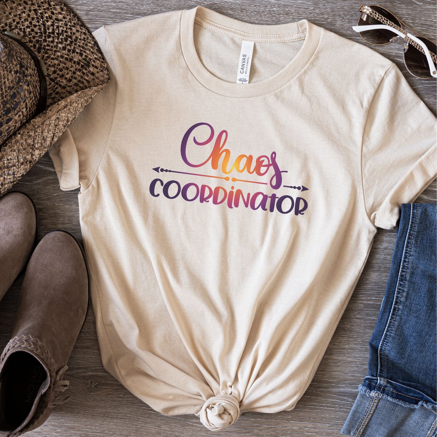 natural color t-shirt laying flat on table with Chaos Coordinator written in colorful multicolored  ink in center of tee.