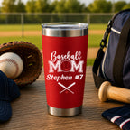 Red tumbler with 'Baseball Mom Stephen #7' text on a wooden surface with baseball equipment.