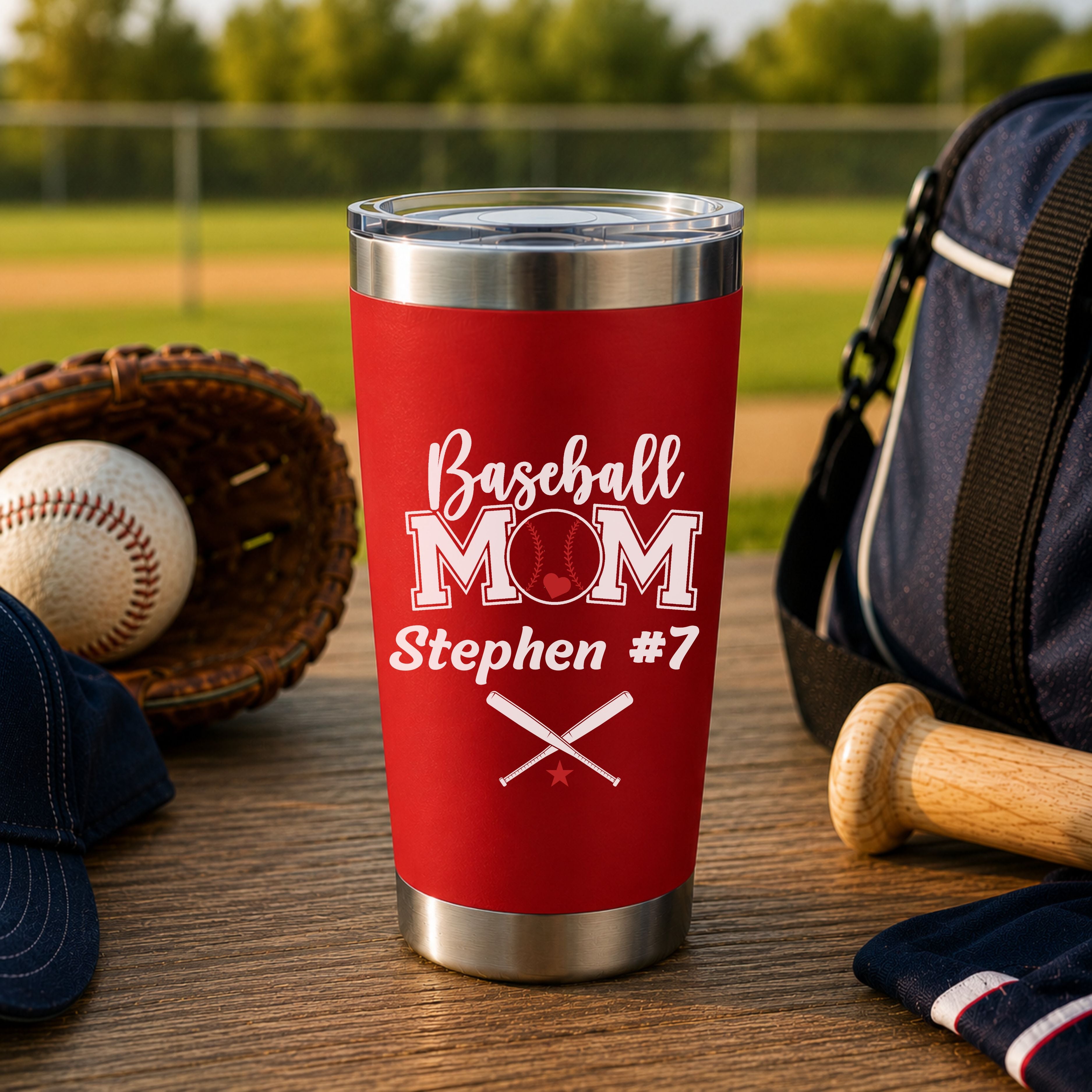 Red tumbler with 'Baseball Mom Stephen #7' text on a wooden surface with baseball equipment.
