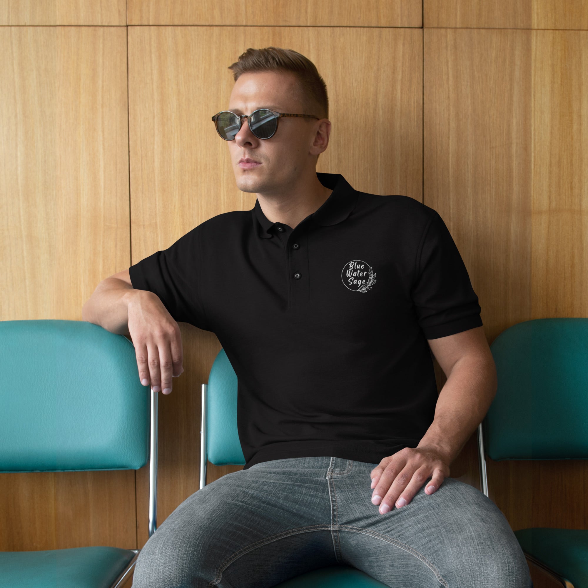 Man wearing a black polo shirt with a logo, sitting against a wooden wall.